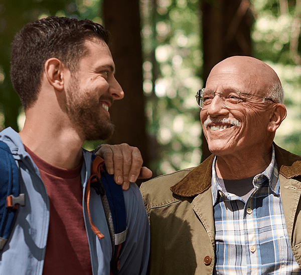 Father and son smiling at each other while hiking in the woods.
